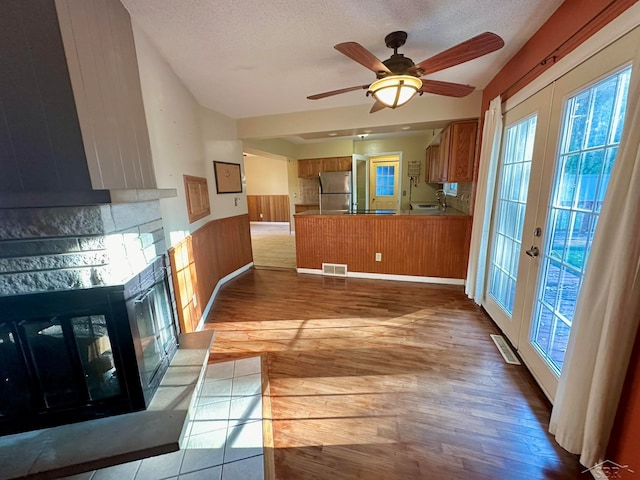 kitchen featuring french doors, light hardwood / wood-style flooring, stainless steel fridge, a textured ceiling, and kitchen peninsula