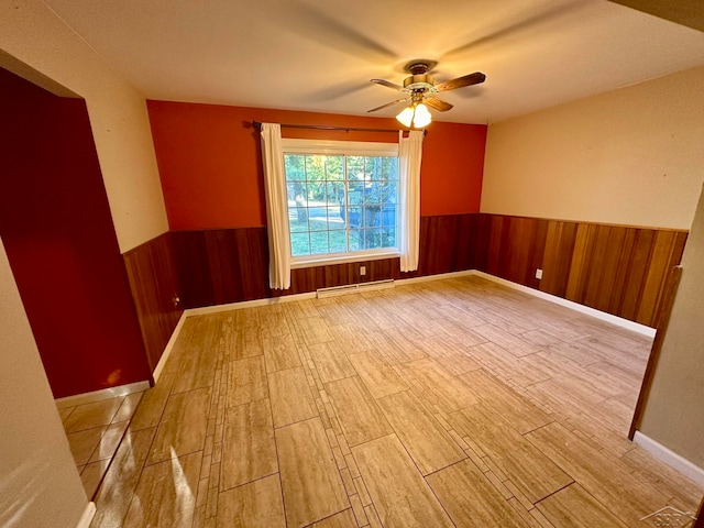 spare room with baseboard heating, ceiling fan, light hardwood / wood-style flooring, and wooden walls