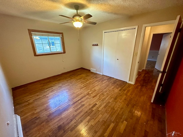 unfurnished bedroom with ceiling fan, dark hardwood / wood-style floors, a textured ceiling, and a closet