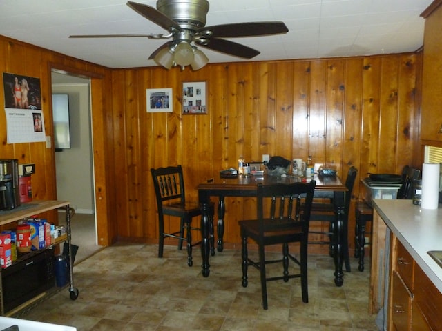 dining area with ceiling fan and wood walls