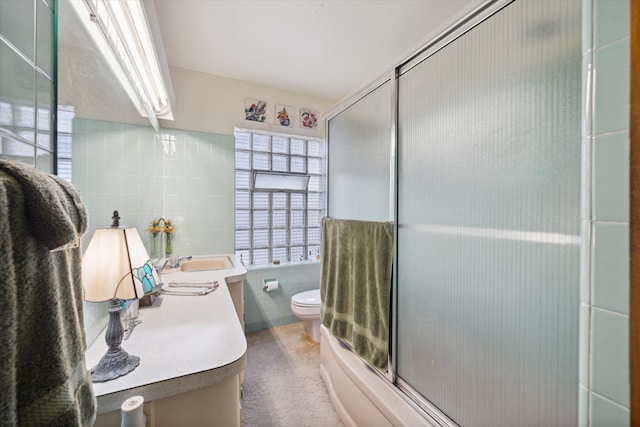 full bathroom featuring vanity, bath / shower combo with glass door, tile walls, and toilet