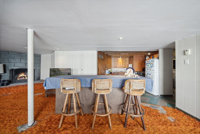 kitchen featuring white refrigerator, a kitchen bar, a fireplace, and wooden walls