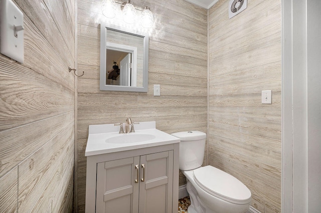 bathroom with vanity, toilet, and wood walls