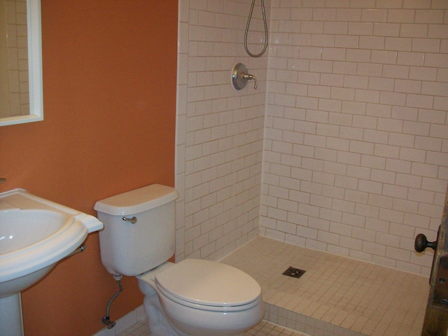 bathroom featuring tile patterned flooring, a tile shower, and toilet