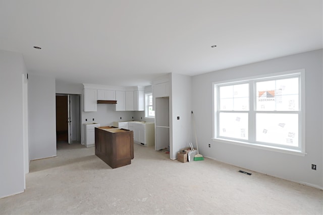 kitchen featuring white cabinets, a center island, light colored carpet, and a wealth of natural light