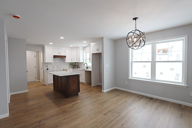 kitchen featuring sink, white cabinetry, hanging light fixtures, a kitchen island, and decorative backsplash