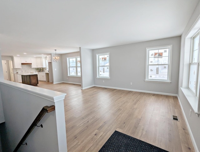 unfurnished living room with sink, a chandelier, and light hardwood / wood-style flooring