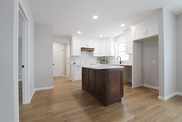 kitchen with sink, white cabinetry, light wood-type flooring, a kitchen island, and backsplash