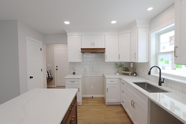 kitchen with tasteful backsplash, sink, white cabinets, light stone countertops, and light wood-type flooring