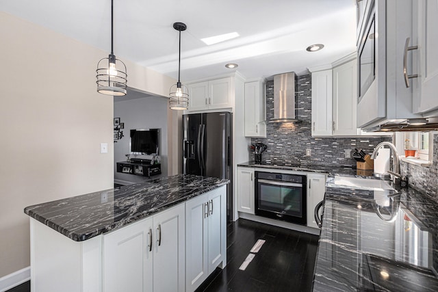 kitchen featuring wall chimney range hood, decorative light fixtures, dark stone countertops, wall oven, and white cabinetry