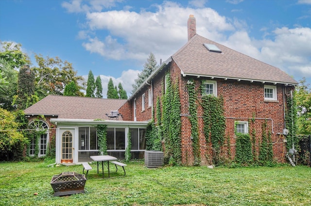 rear view of house featuring a sunroom, a yard, cooling unit, and an outdoor fire pit