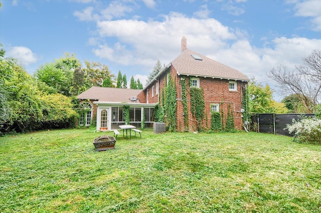 back of house with central AC, a sunroom, a yard, and an outdoor fire pit