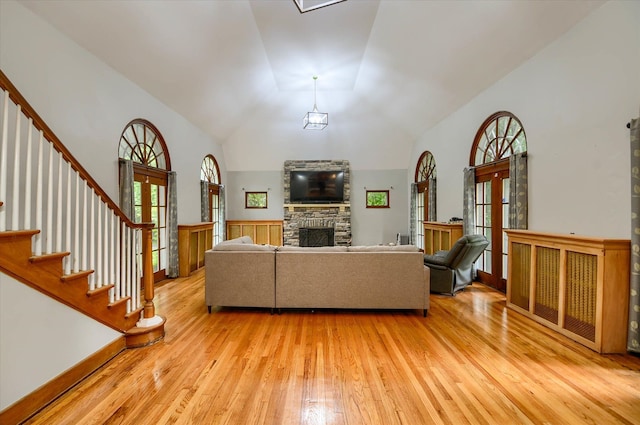 living room featuring a fireplace, french doors, light wood-type flooring, and high vaulted ceiling