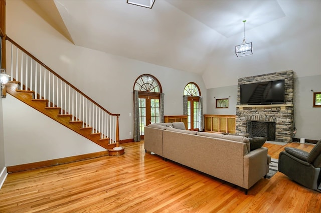 living room featuring high vaulted ceiling, an inviting chandelier, french doors, light wood-type flooring, and a fireplace