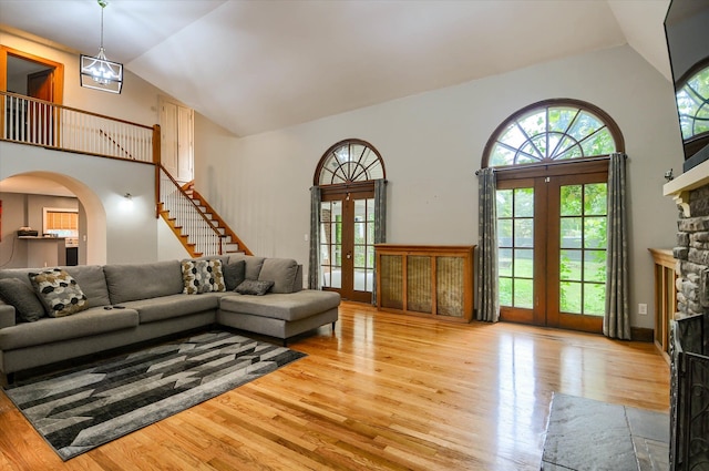 living room with french doors, light wood-type flooring, high vaulted ceiling, and a stone fireplace