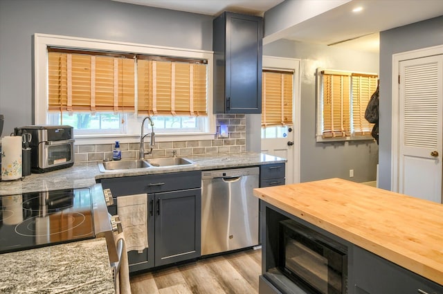 kitchen featuring light stone countertops, appliances with stainless steel finishes, light wood-type flooring, tasteful backsplash, and sink