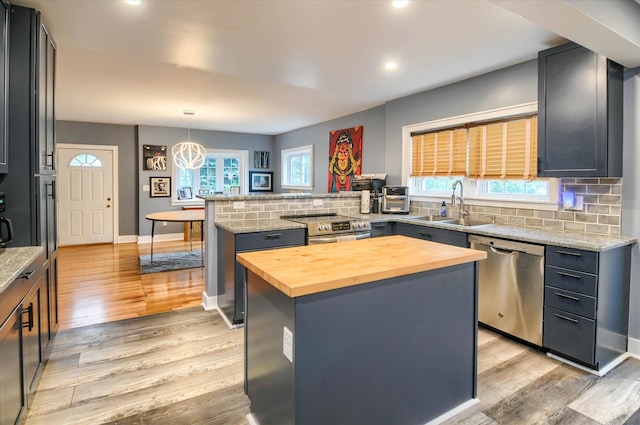 kitchen with stainless steel appliances, sink, decorative light fixtures, light hardwood / wood-style floors, and a kitchen island