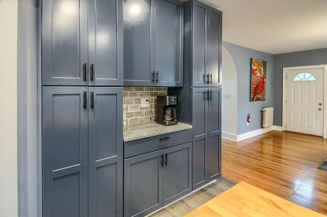 kitchen featuring light stone countertops, decorative backsplash, radiator heating unit, and light hardwood / wood-style floors