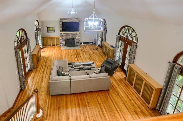 living room featuring lofted ceiling, light hardwood / wood-style floors, an inviting chandelier, and a stone fireplace