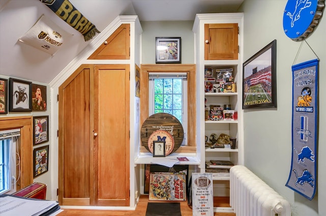 hallway featuring vaulted ceiling, radiator heating unit, and light hardwood / wood-style flooring