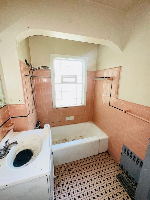 bathroom with radiator, vanity, tiled shower / bath combo, and tile walls