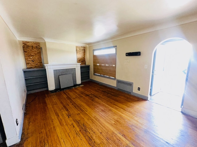 unfurnished living room featuring dark hardwood / wood-style floors, radiator heating unit, and a brick fireplace