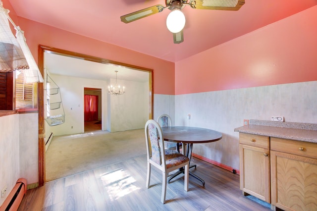 dining room with light wood-type flooring, ceiling fan with notable chandelier, and a baseboard heating unit