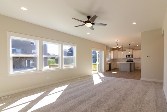 unfurnished living room featuring ceiling fan with notable chandelier and light colored carpet