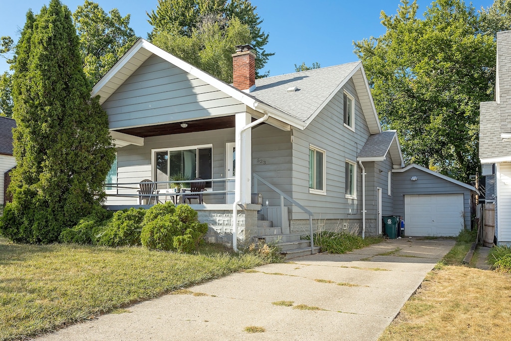 bungalow-style home featuring a front lawn, covered porch, an outdoor structure, and a garage