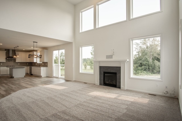 unfurnished living room with a tile fireplace, sink, a towering ceiling, a chandelier, and light colored carpet