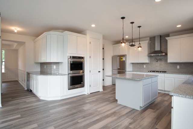 kitchen featuring wood-type flooring, stainless steel appliances, white cabinetry, and wall chimney exhaust hood