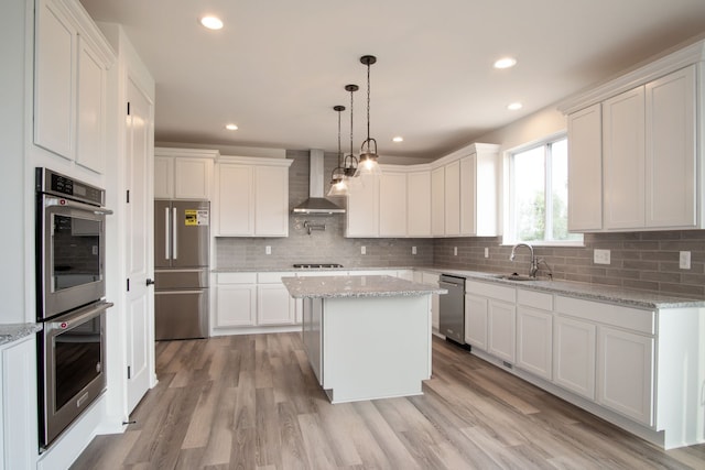 kitchen with a kitchen island, wall chimney range hood, stainless steel appliances, and white cabinetry