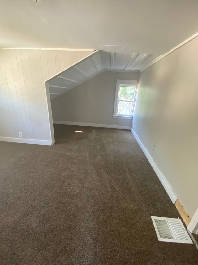 additional living space with dark colored carpet and vaulted ceiling