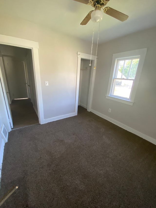 unfurnished bedroom with dark colored carpet, a closet, and ceiling fan