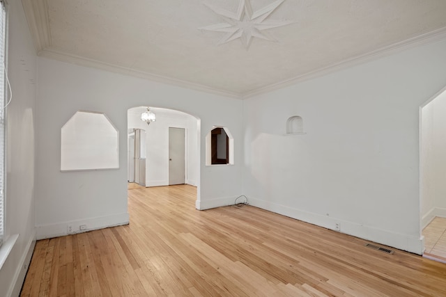 empty room featuring an inviting chandelier, ornamental molding, and light wood-type flooring