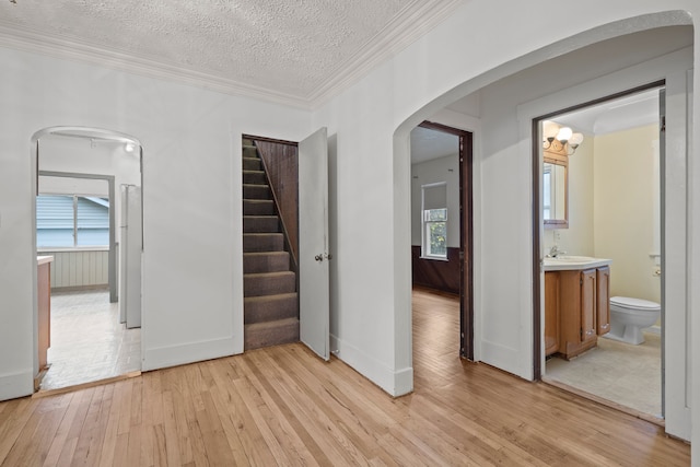 unfurnished bedroom featuring ornamental molding, a textured ceiling, an inviting chandelier, light hardwood / wood-style flooring, and connected bathroom