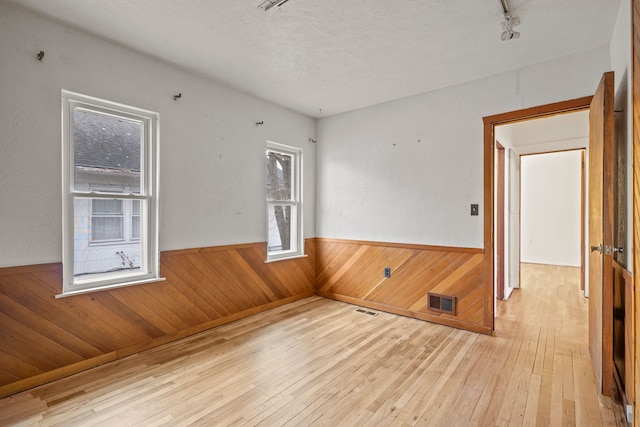 unfurnished room with a textured ceiling, light hardwood / wood-style flooring, and wooden walls