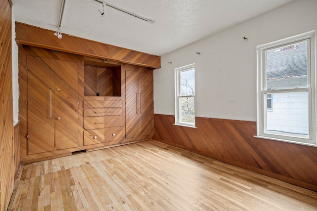 unfurnished room with hardwood / wood-style flooring, a textured ceiling, wooden walls, and track lighting