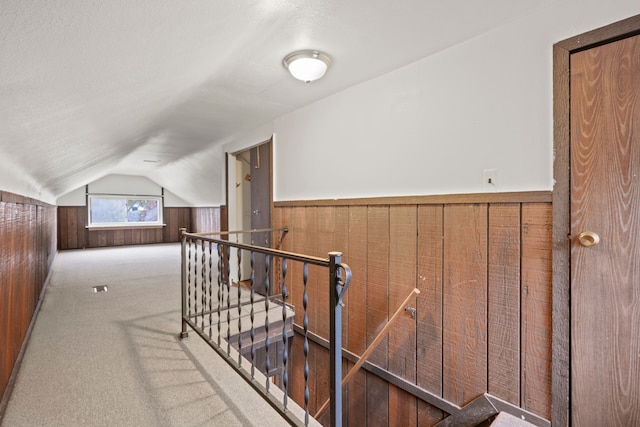 corridor with a textured ceiling, wood walls, carpet floors, and lofted ceiling