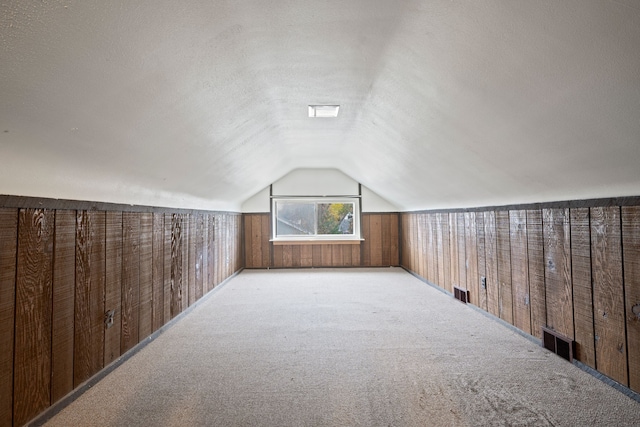 bonus room with wood walls, light colored carpet, a textured ceiling, and vaulted ceiling