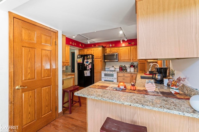 kitchen with rail lighting, black fridge, white range, kitchen peninsula, and a kitchen bar