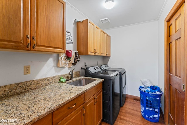 laundry room featuring cabinets, ornamental molding, sink, washing machine and dryer, and light hardwood / wood-style floors