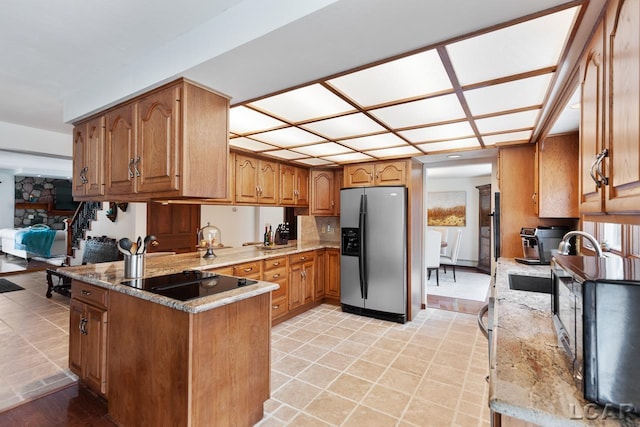 kitchen featuring kitchen peninsula, stainless steel refrigerator with ice dispenser, light stone countertops, black electric cooktop, and sink