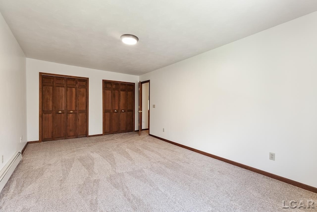 unfurnished bedroom featuring two closets, baseboard heating, and light colored carpet