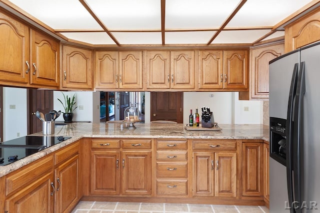 kitchen featuring kitchen peninsula, light stone counters, black electric cooktop, and stainless steel refrigerator with ice dispenser