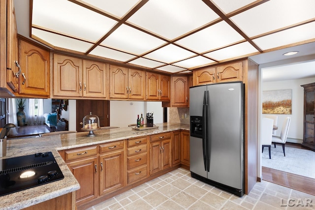 kitchen featuring kitchen peninsula, stainless steel refrigerator with ice dispenser, light stone countertops, black electric stovetop, and sink