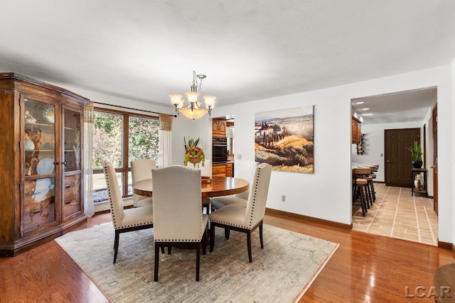 dining area with light hardwood / wood-style floors, a baseboard radiator, and an inviting chandelier