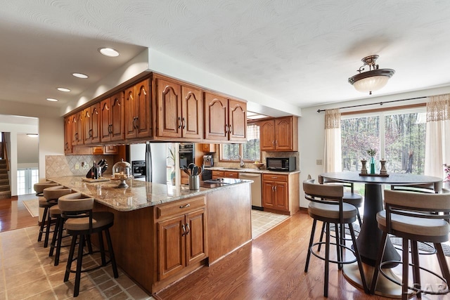 kitchen featuring kitchen peninsula, a kitchen breakfast bar, tasteful backsplash, black appliances, and light hardwood / wood-style floors