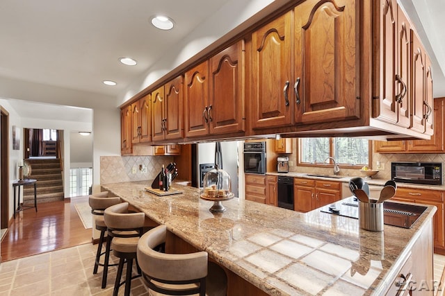 kitchen with black appliances, a kitchen breakfast bar, sink, tasteful backsplash, and light hardwood / wood-style floors