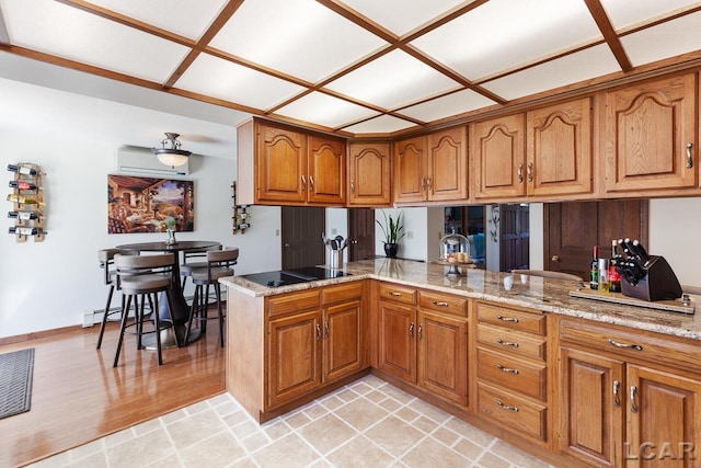 kitchen featuring light stone countertops, a baseboard radiator, kitchen peninsula, black electric cooktop, and light wood-type flooring